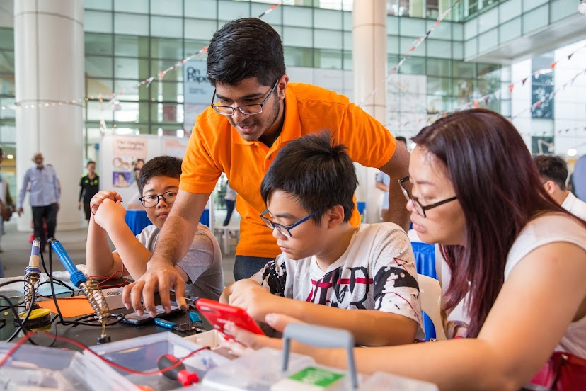 Photo from T4G 2019 Assistive Switch workshop where a volunteer is going through the instructions with 3 participants
